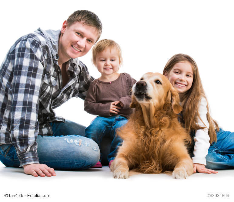 Ein liegender Hund und um ihn herum sitzen zwei Kinder und ein Mann und streicheln ihn.