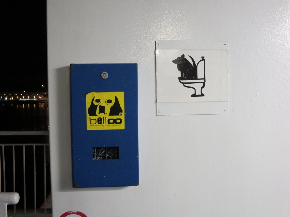Ein Schild mit einem Hund auf einer Toilette und eine Box mit Abfallbeuteln für das Geschäft