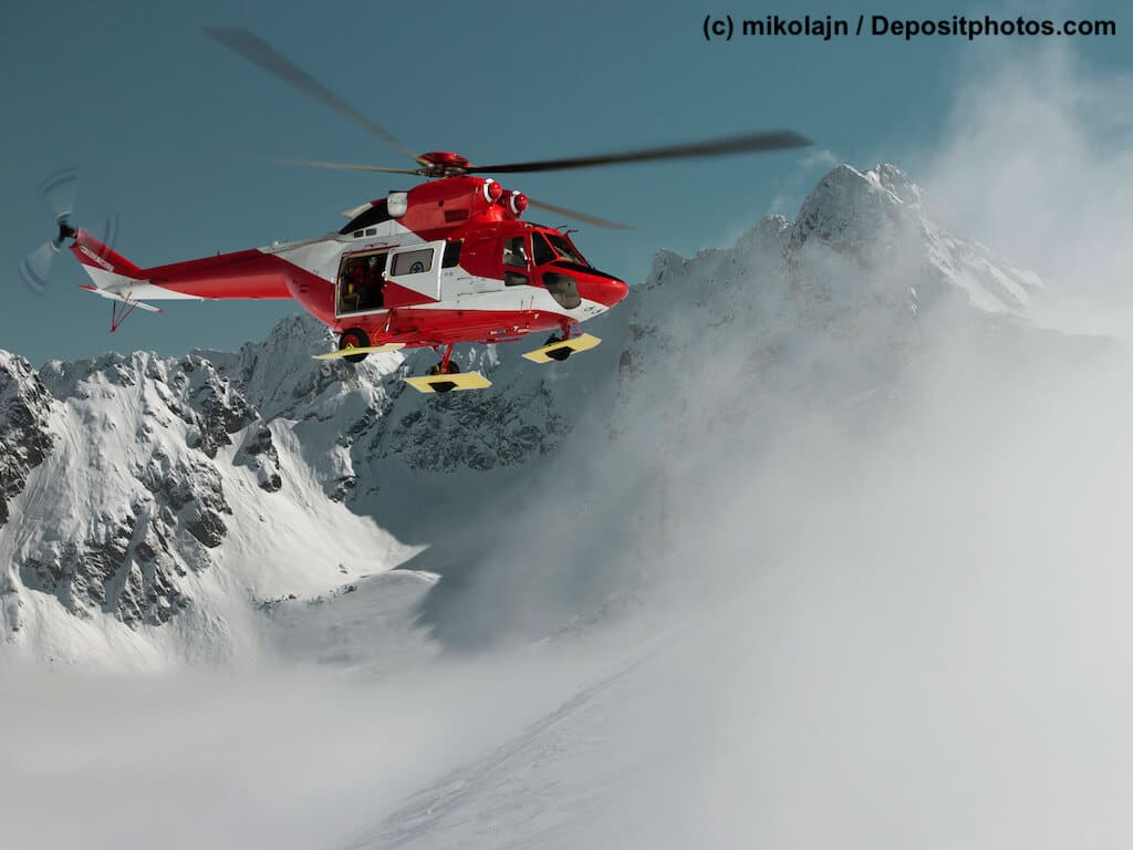 Ein rotweiĂer Helikopter steuert verschneiten Berghang an