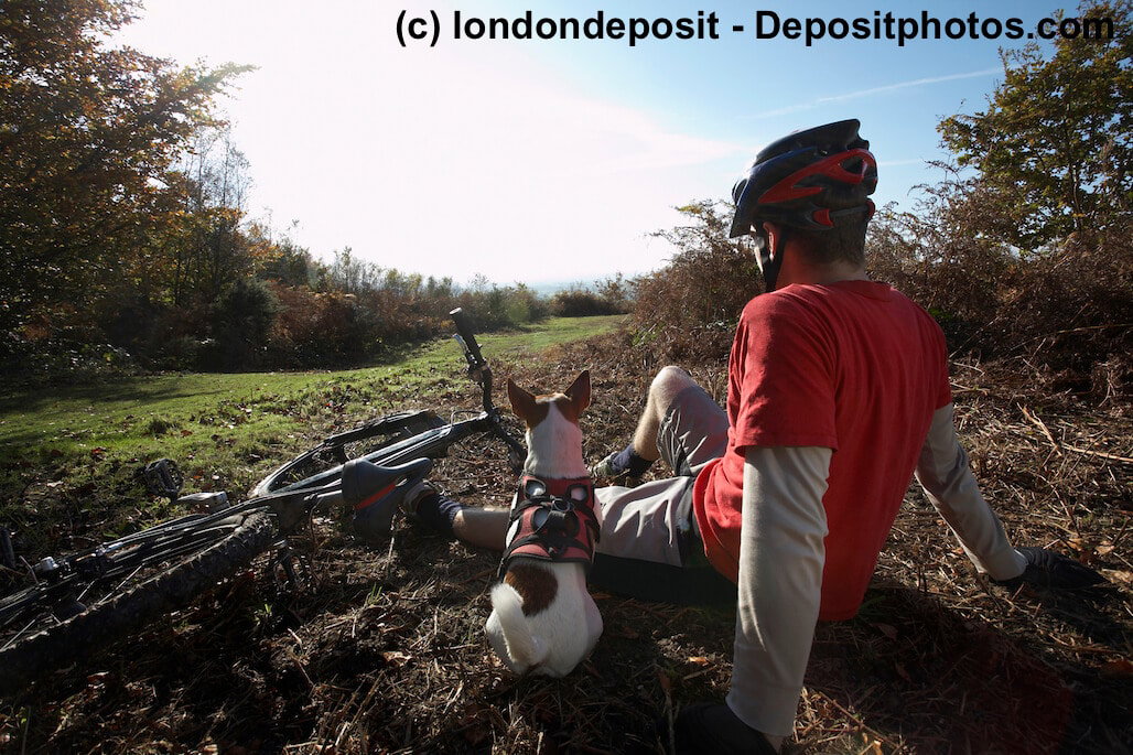 Ein Mountain biker und sein Hund sitzen nebeneinander und schauen in die Landschaft