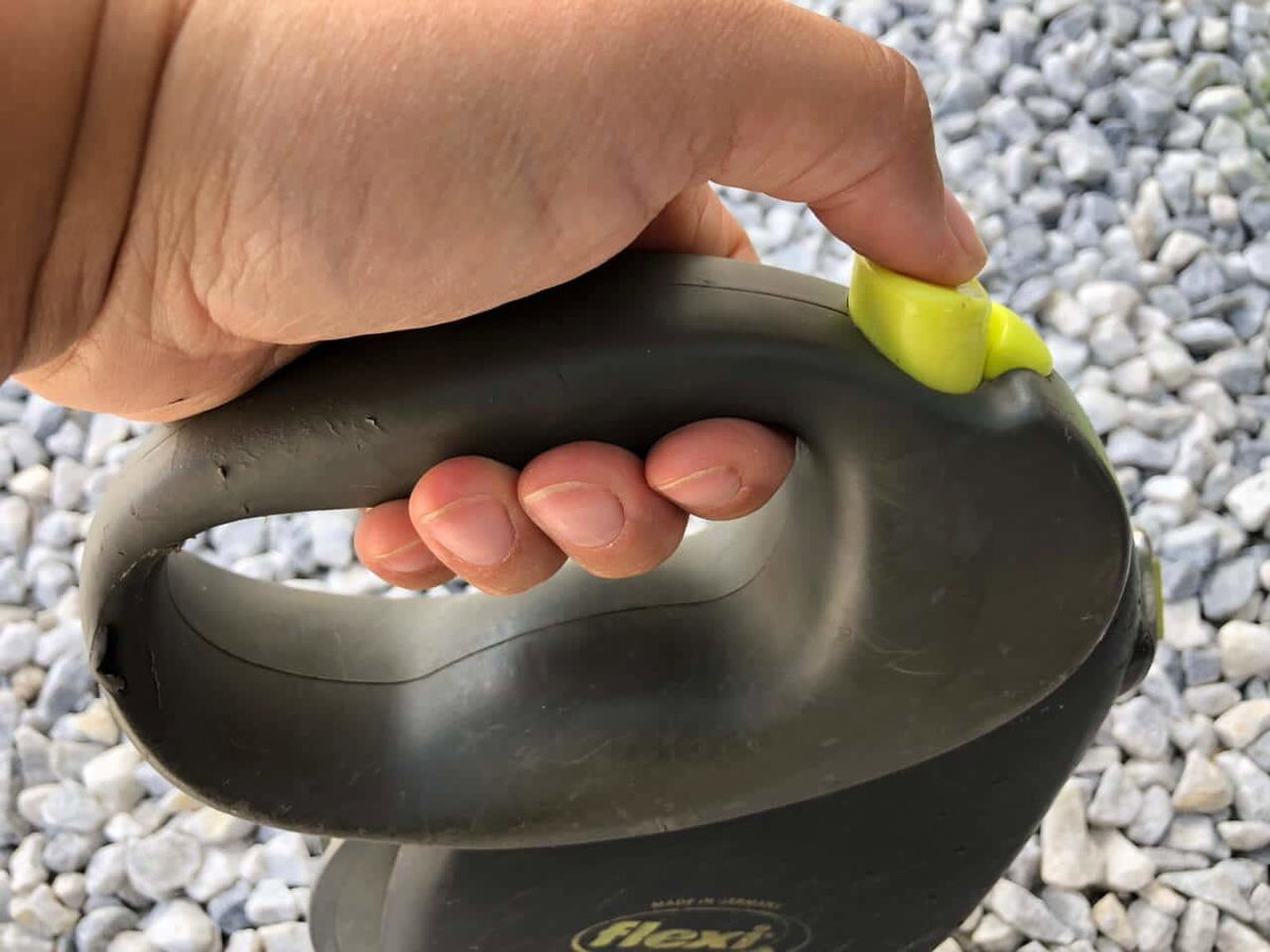 Blick von der Seite auf eine Flexileine mit dem Daumen auf der Bremse