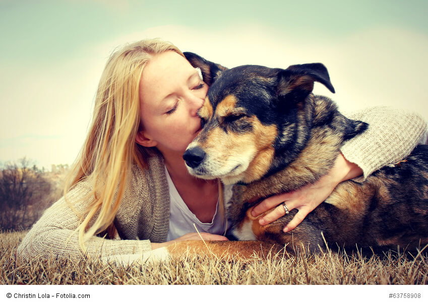 Eine blonde junge Frau umarmt und küsst ihren Deutschen Schäferhund